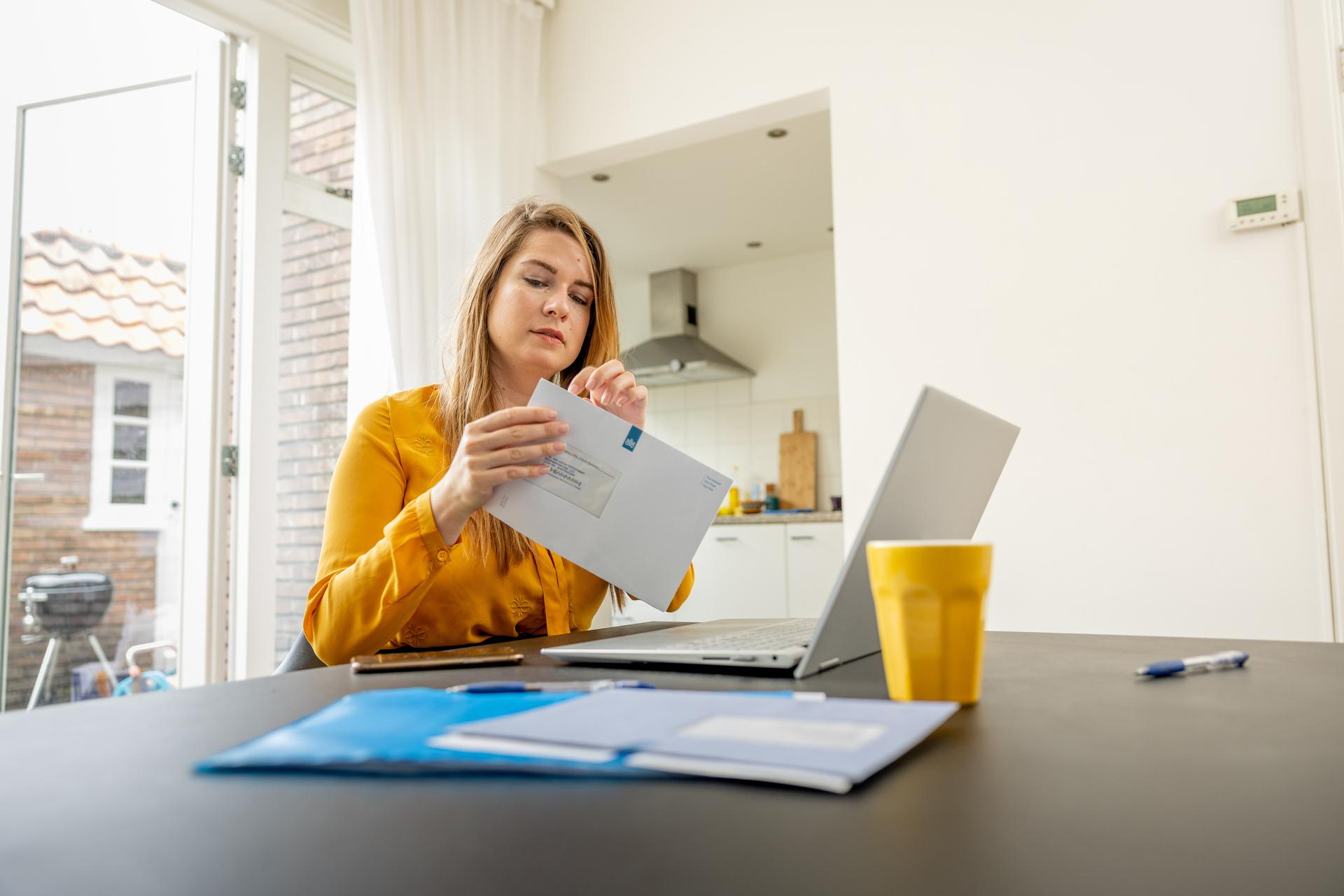 afbeelding ter illustratie: vrouw aan tafel met laptop en brief